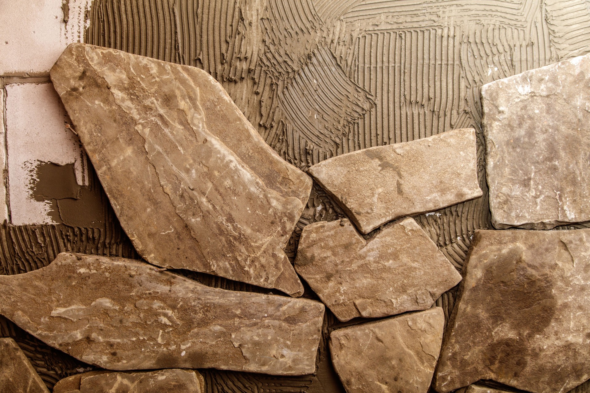 A wall is being tiled with a brown stone