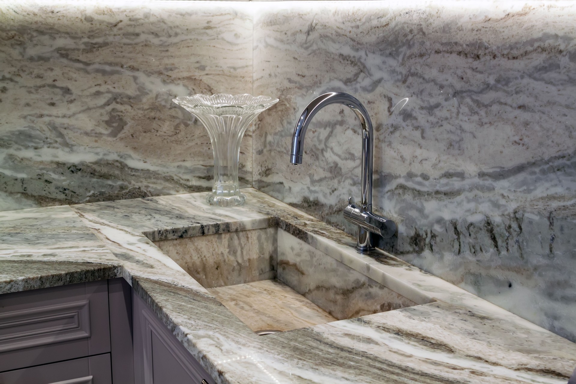New modern faucet and kitchen sink close up made of stone as well as granite countertops in apartment. Close up view of chrome faucet and marble sink